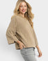 Woman wearing a beige sweater and gray jeans on a white background