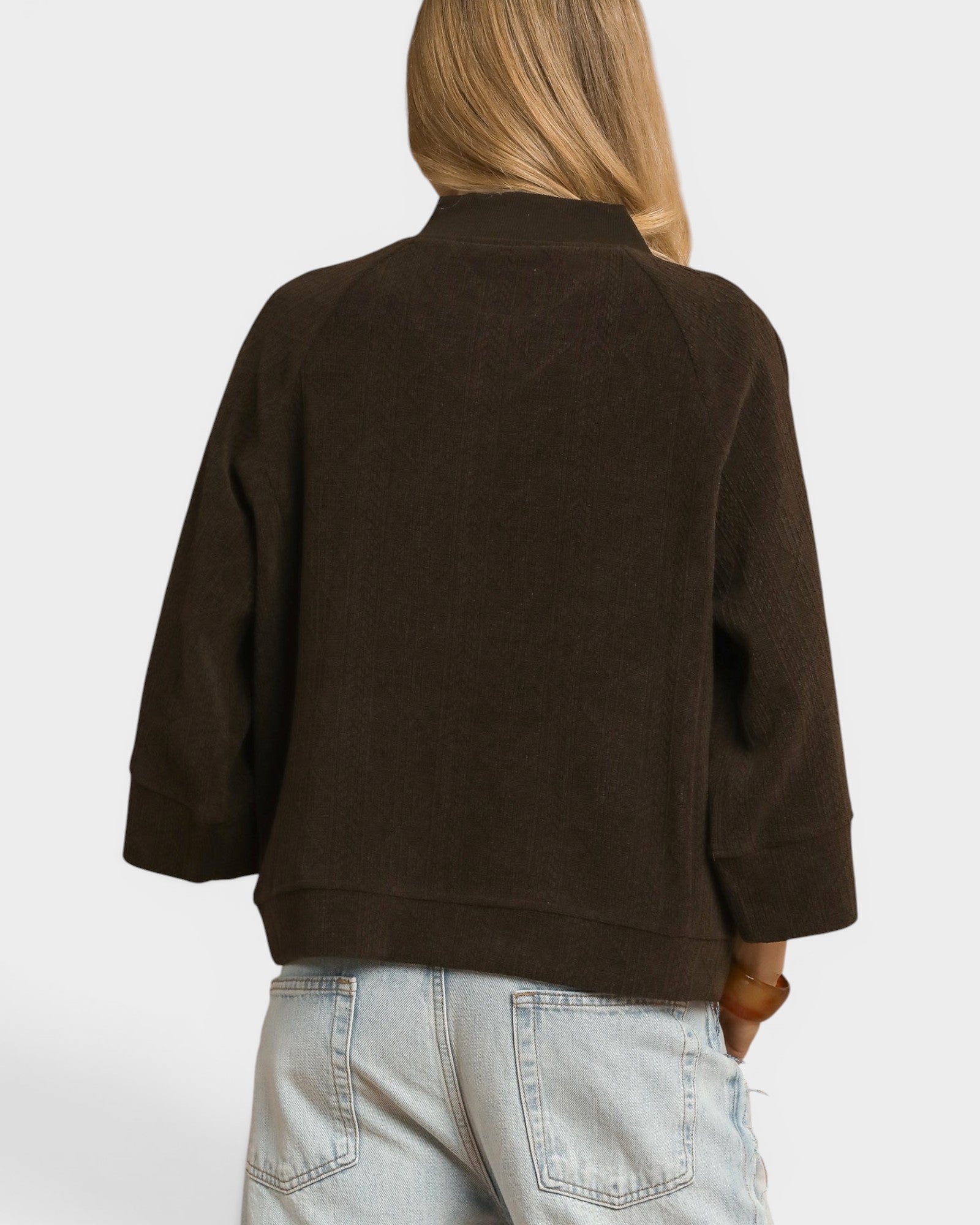 Person wearing a brown sweater and light blue jeans on a white background