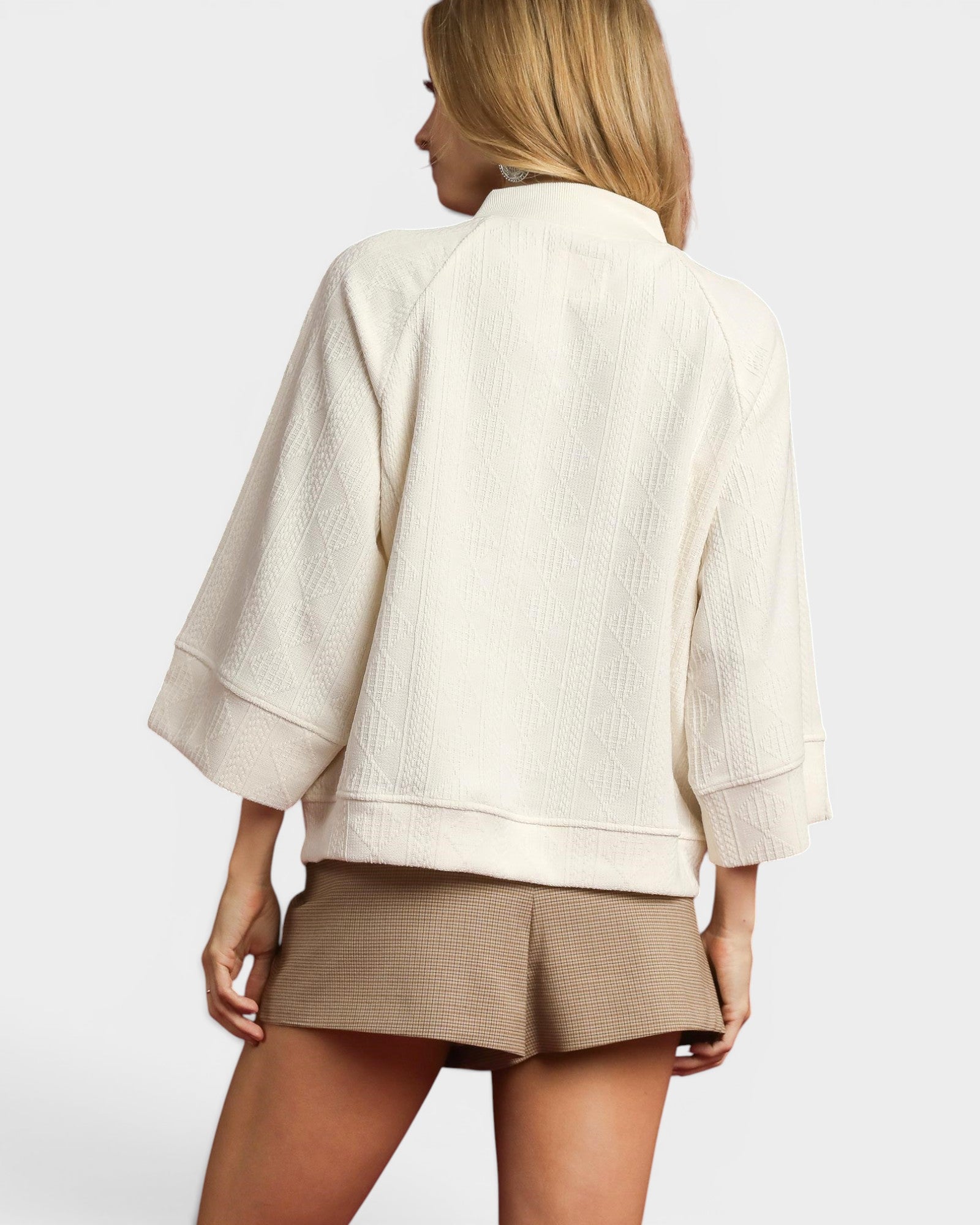 Woman wearing a beige top and shorts on a plain background