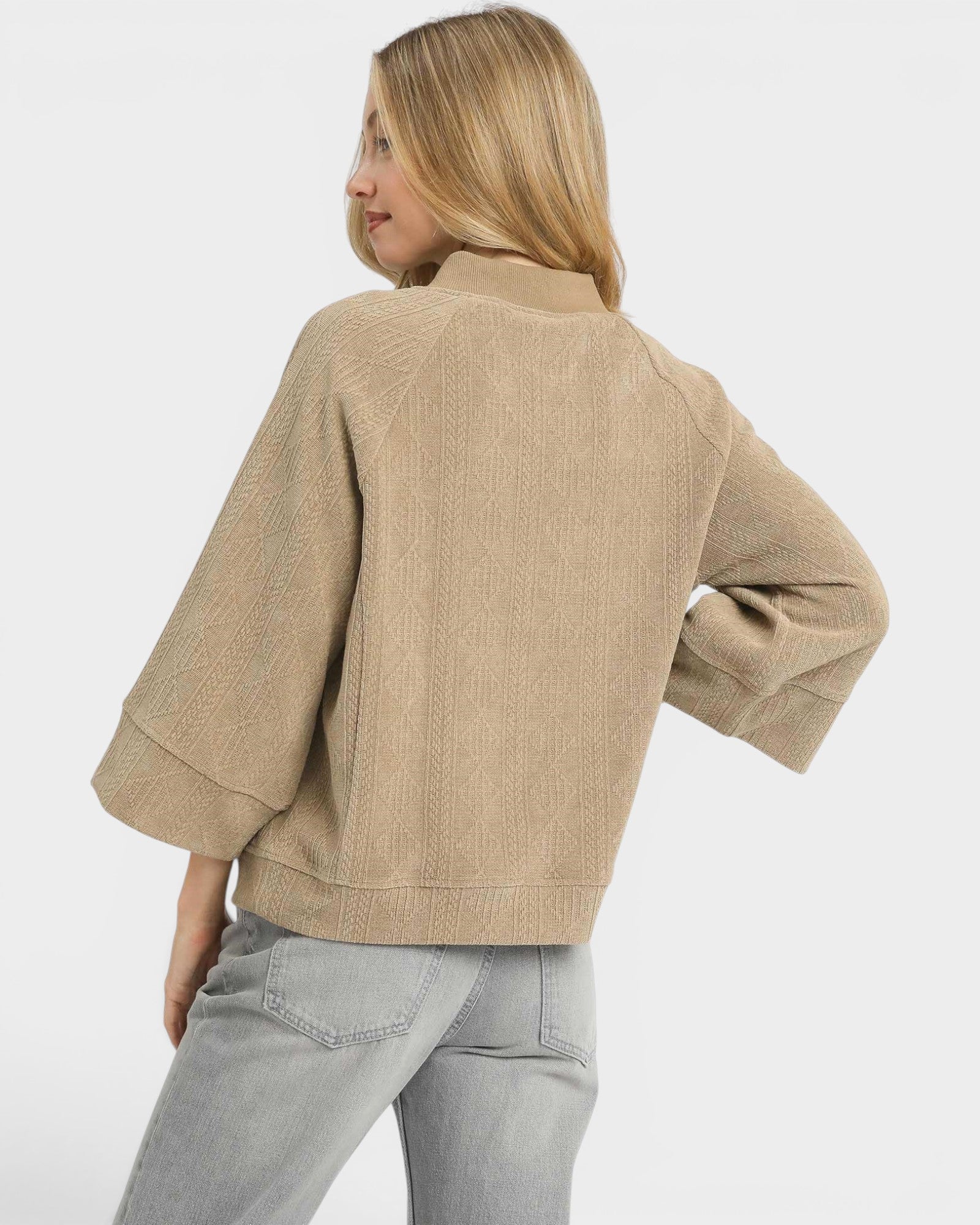 Woman wearing a beige sweater and light gray pants on a white background