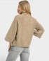 Woman wearing a beige sweater and light gray pants on a white background