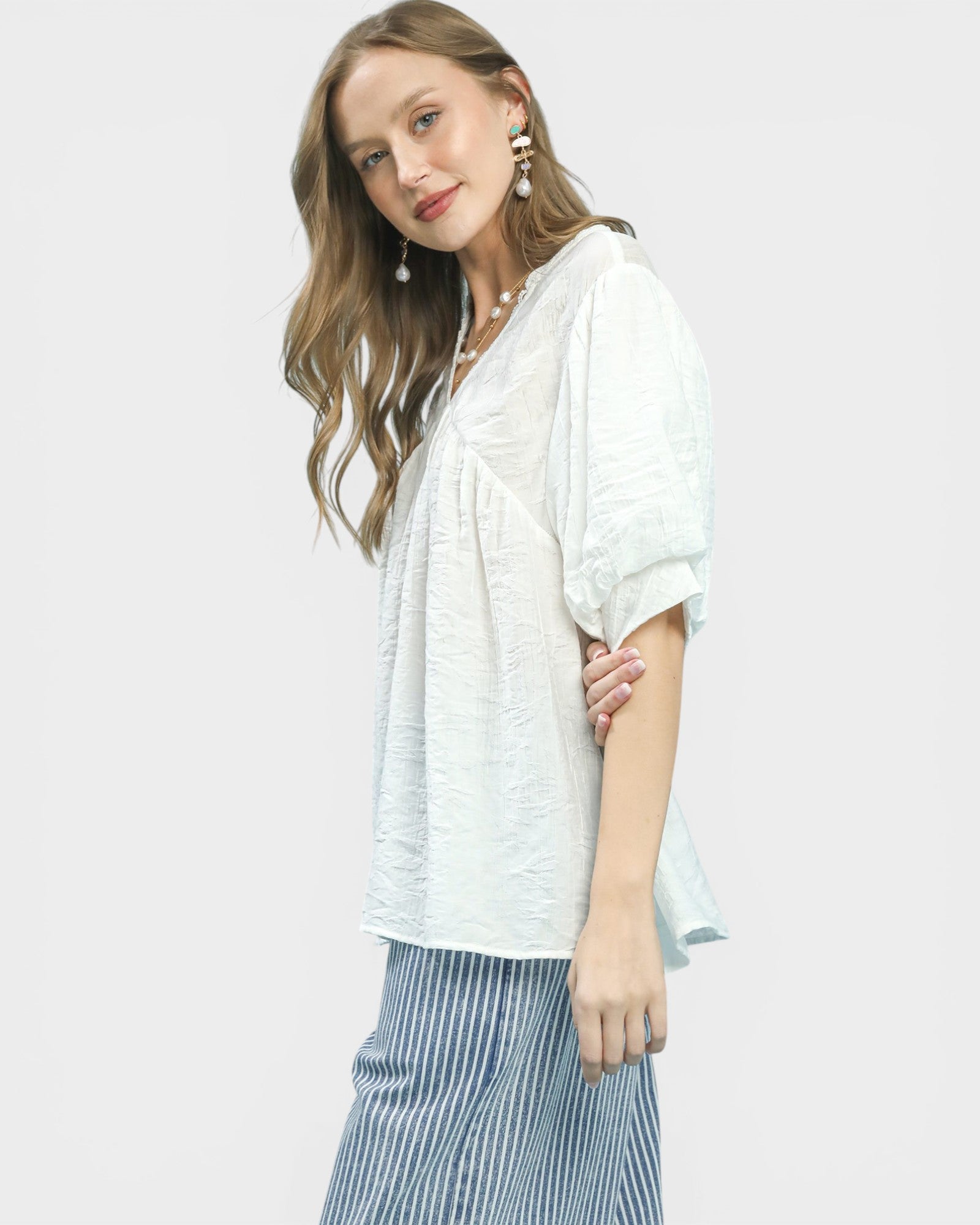Woman wearing a white blouse and striped pants on a light gray background
