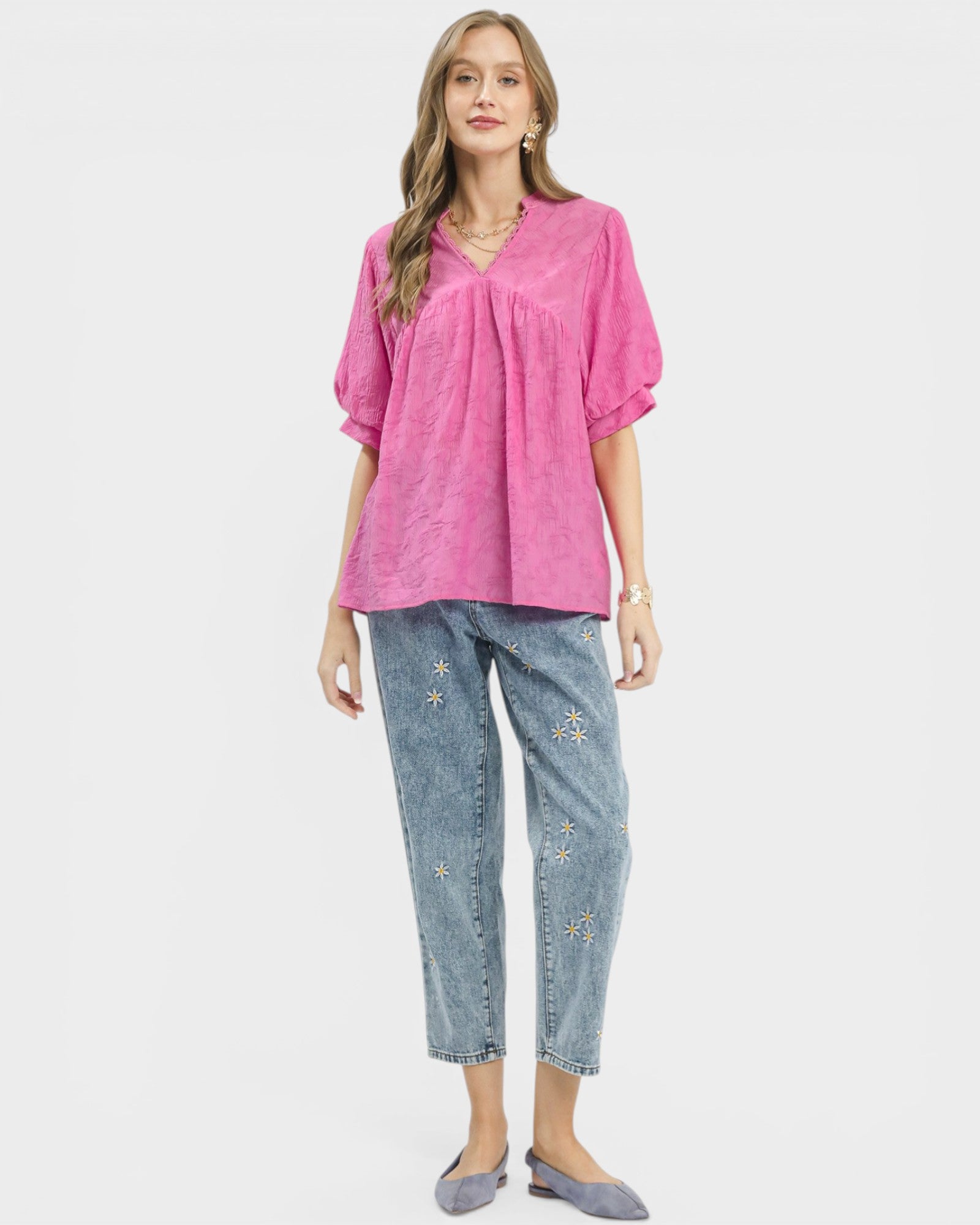 Woman wearing a pink blouse and blue jeans with floral embroidery on a white background