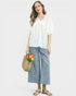 Woman wearing a white blouse and blue striped pants, holding a straw bag with flowers on a white background