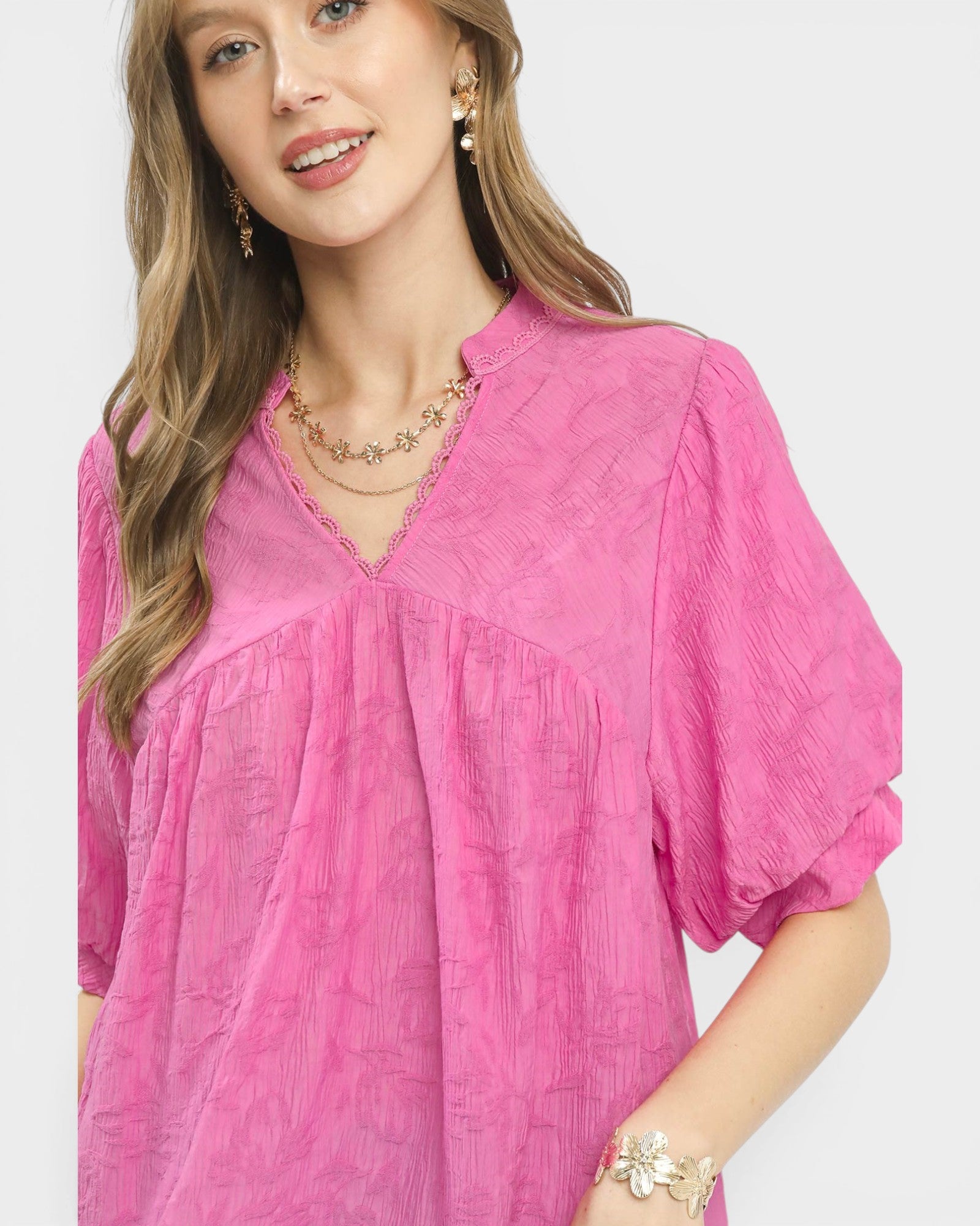 Woman wearing a pink blouse with gold jewelry on a white background