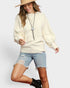 Woman wearing a cream sweater, denim shorts, and a beige hat on a white background