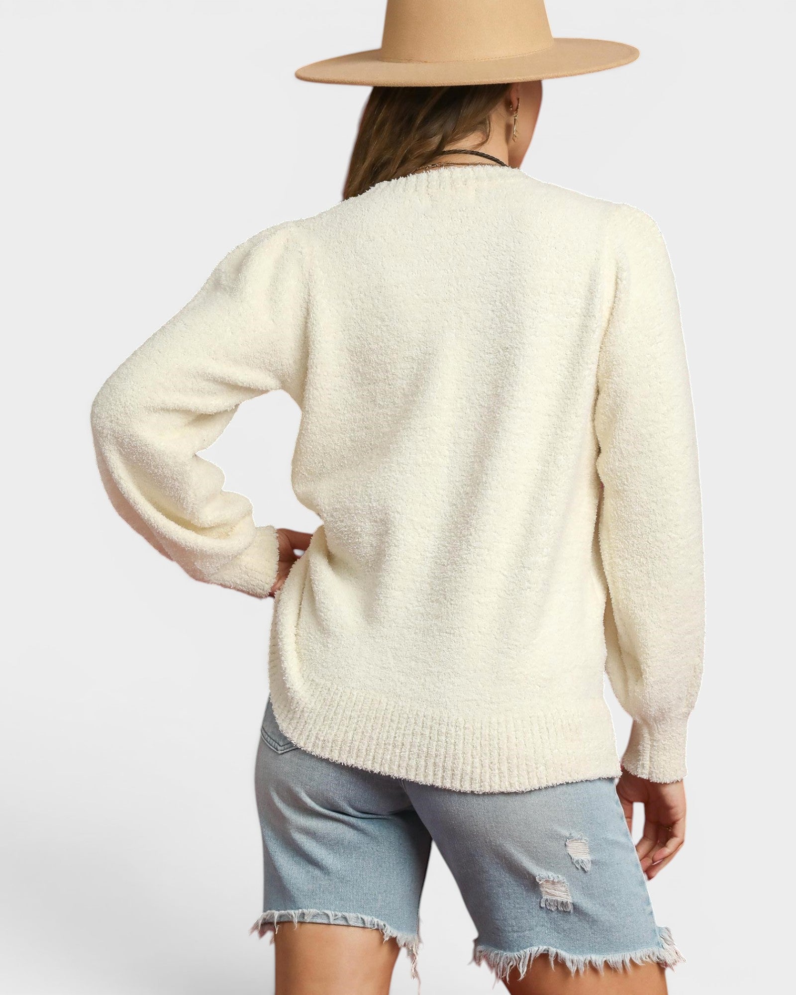Person wearing a cream sweater and denim shorts with a beige hat on a light gray background