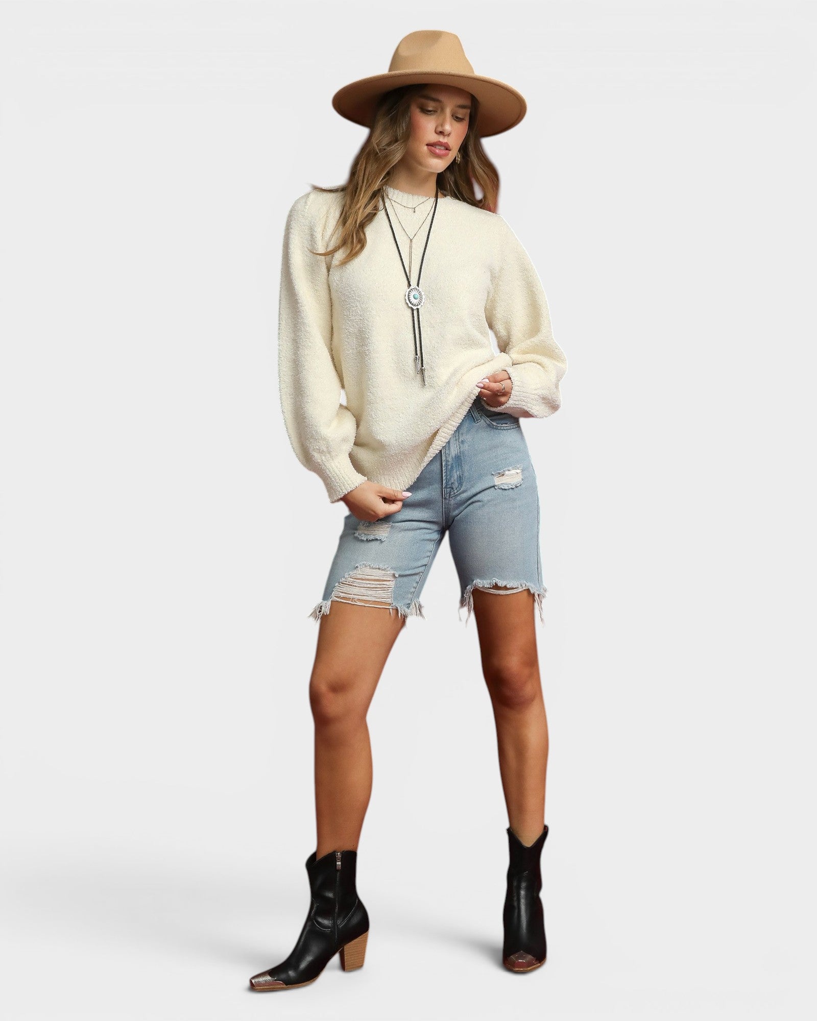 Woman wearing a cream sweater, denim shorts, and black boots on a white background