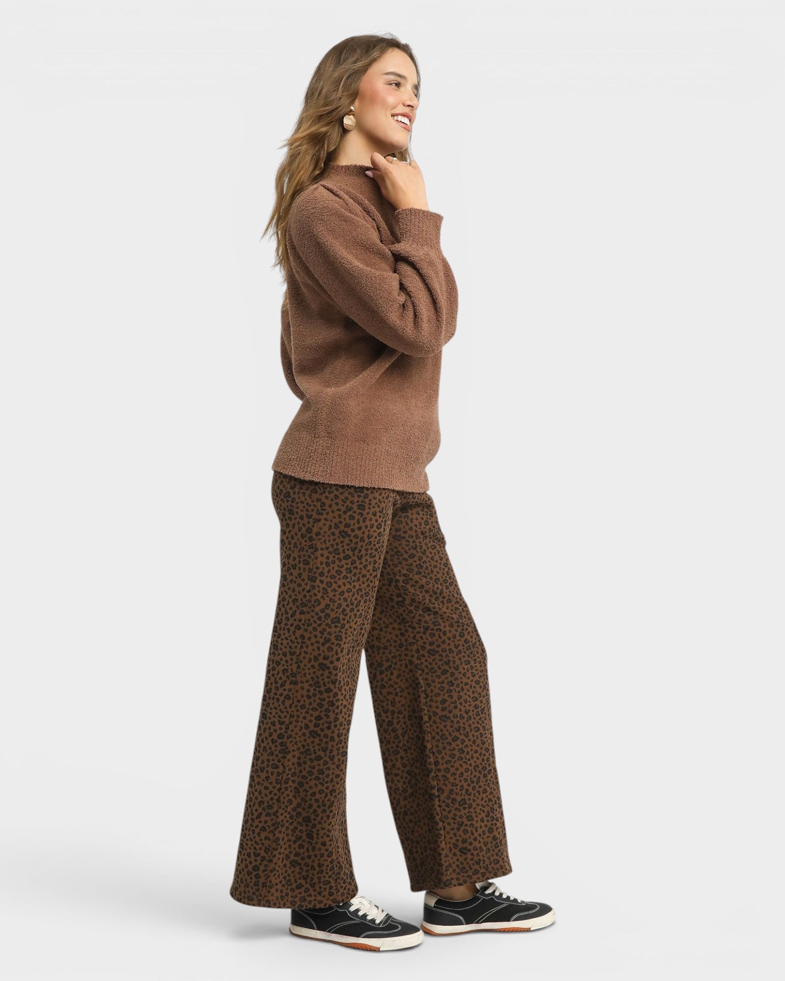 Woman wearing a brown sweater and leopard print pants on a white background