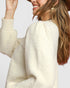 Woman wearing a cream-colored sweater with a plain background