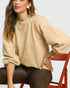 Woman wearing a beige sweater sitting on a red chair against a white background