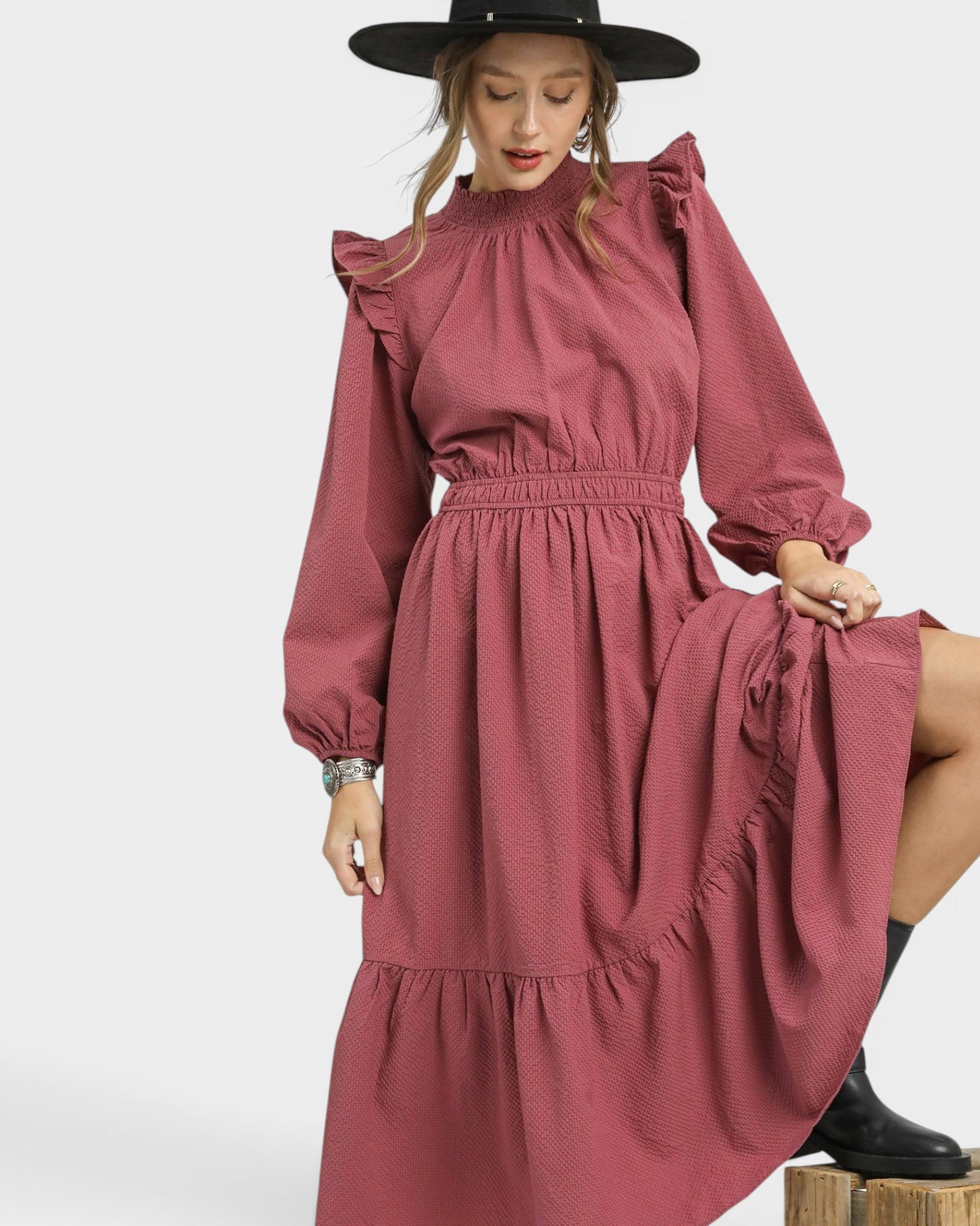 Woman wearing a pink dress with ruffled sleeves and a black hat on a white background