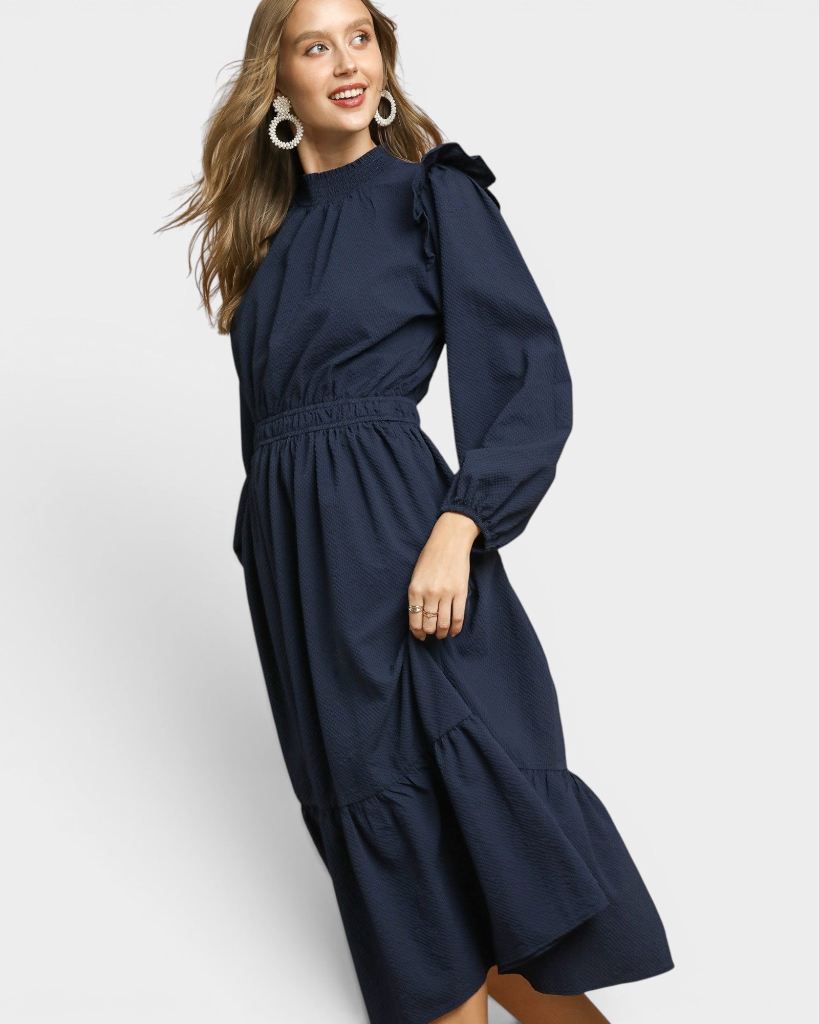 Woman wearing a navy blue dress with long sleeves and a belt on a white background