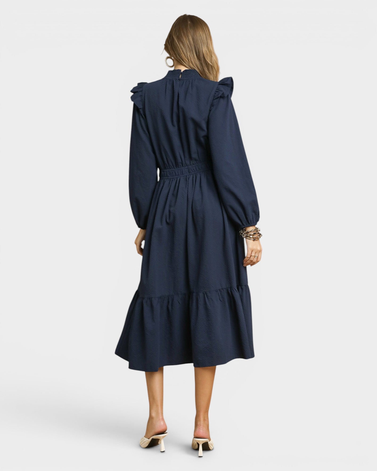 Woman wearing a navy blue dress with long sleeves and a belt on a white background