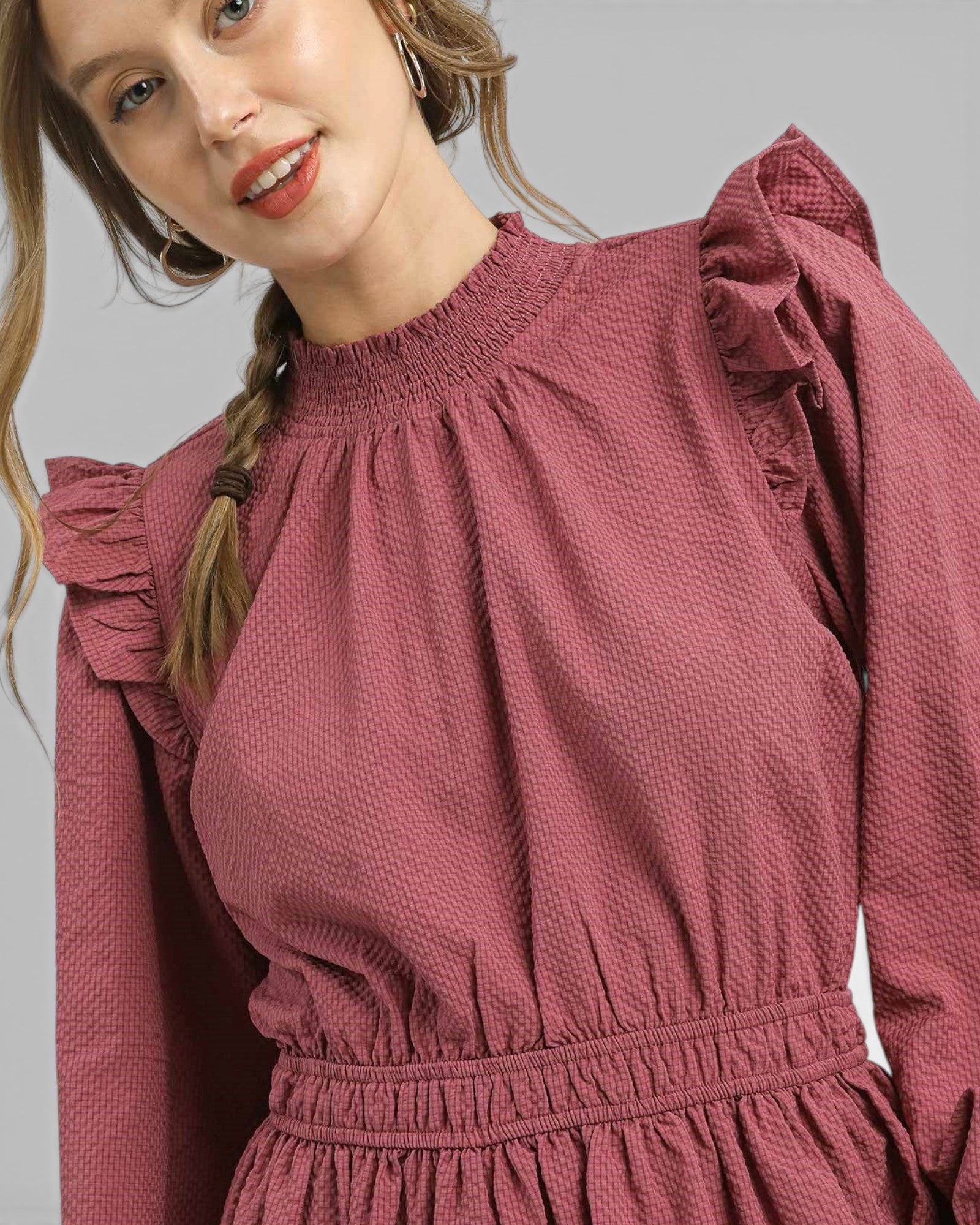 Woman wearing a pink dress with ruffled sleeves against a gray background