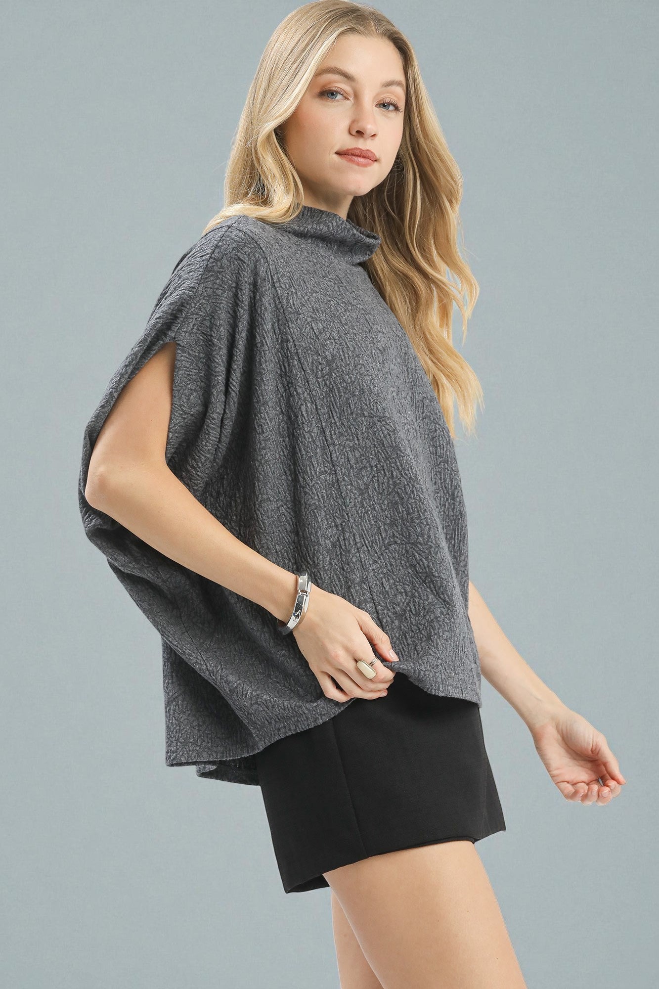 Woman wearing a gray poncho over a black outfit on a gray background