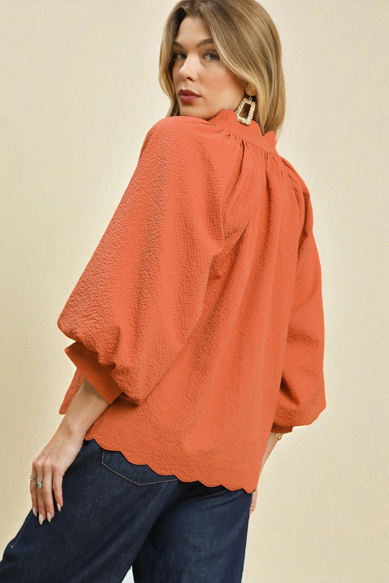 Woman wearing an orange blouse with scalloped edges on a beige background