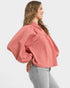 Woman wearing a pink textured blouse and gray pants on a white background