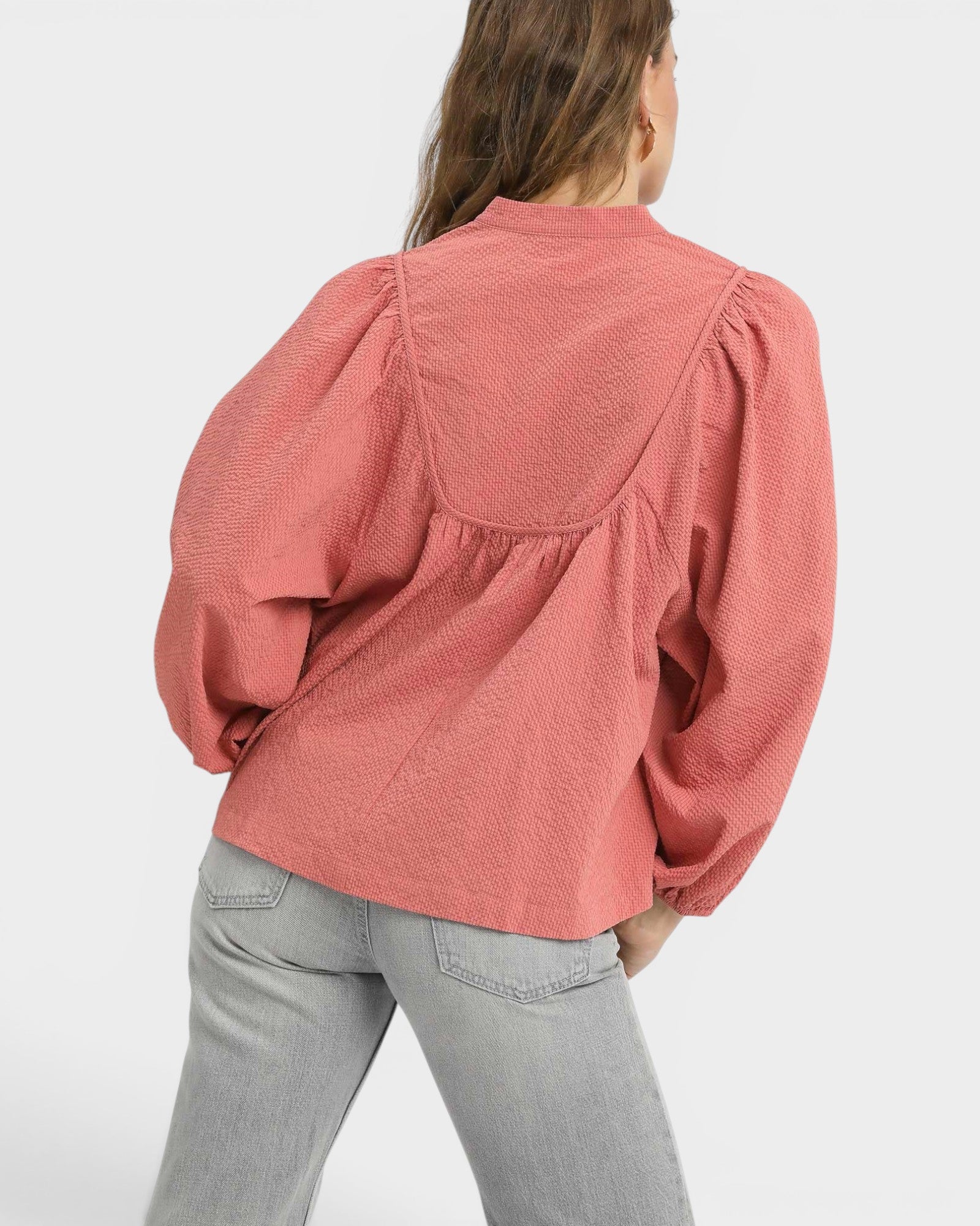 Person wearing a pink textured blouse and light gray pants on a white background