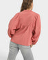 Person wearing a pink textured blouse and light gray pants on a white background