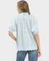 Woman wearing a light blue blouse with scalloped edges on a white background