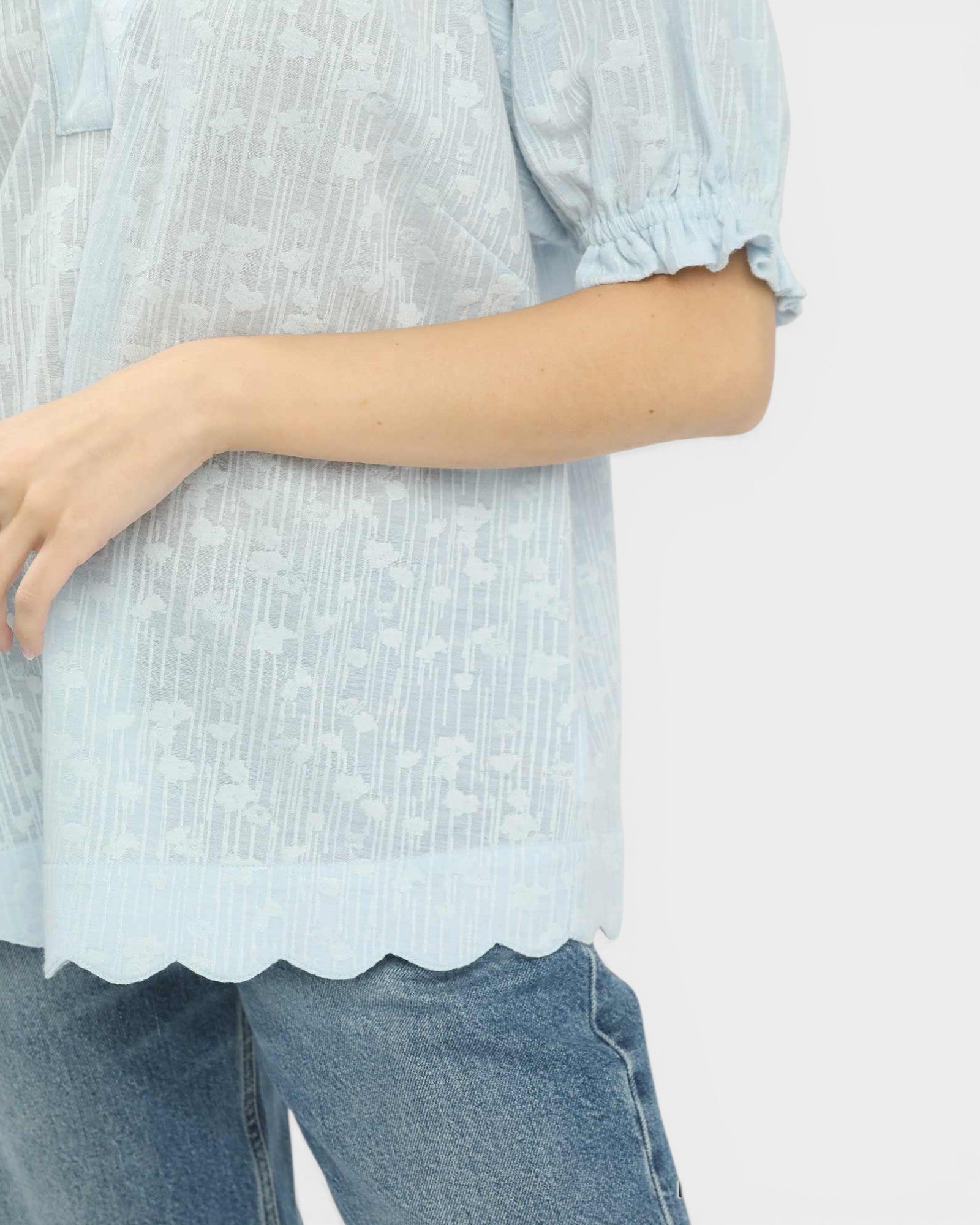 Light blue textured blouse worn by a person on a white background