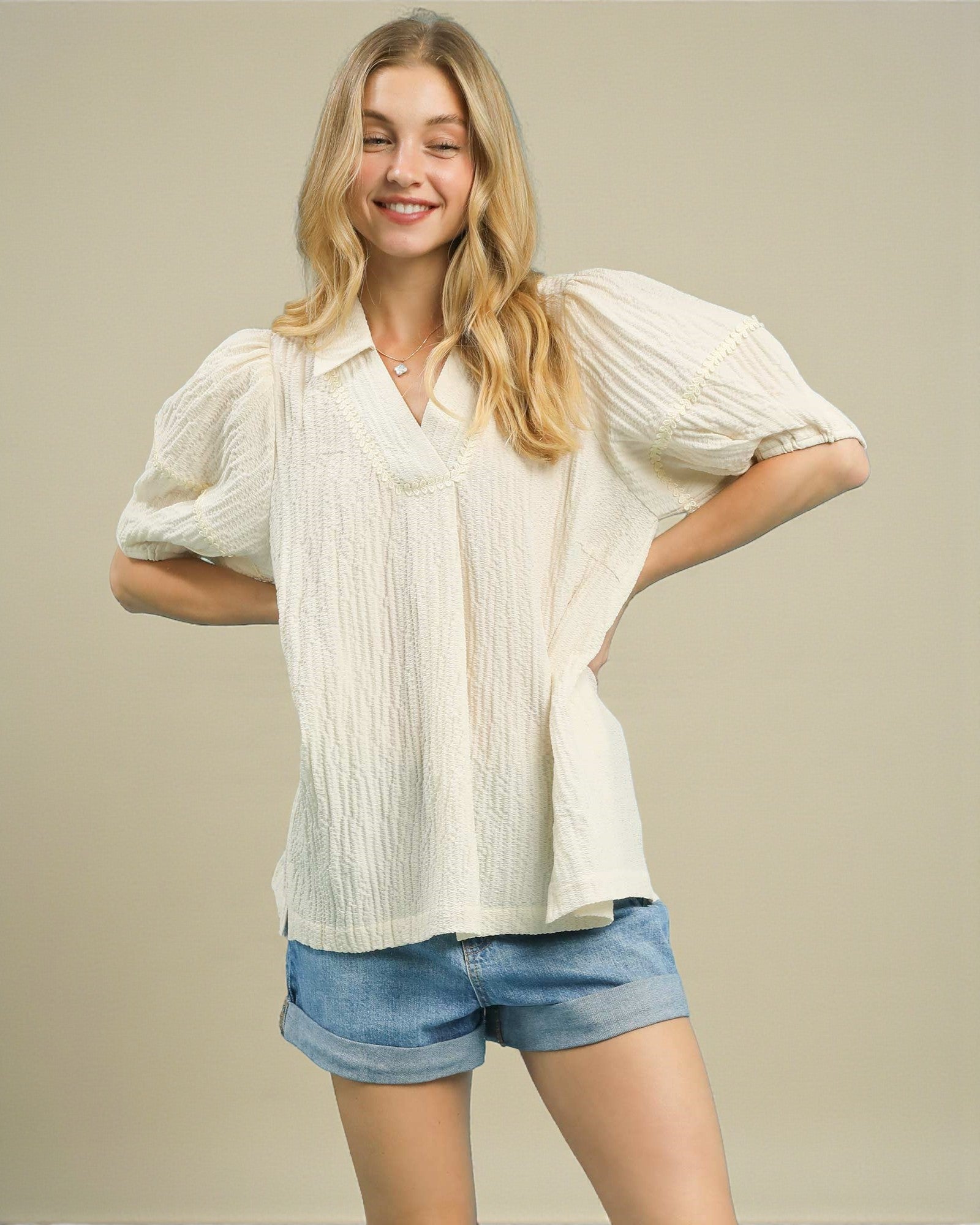 Woman wearing a white blouse with puffed sleeves and denim shorts on a beige background