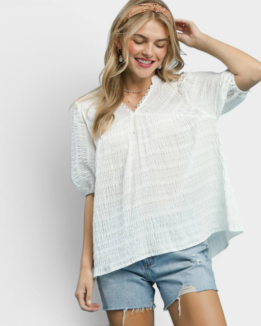 Woman wearing a white textured blouse and denim shorts on a plain background
