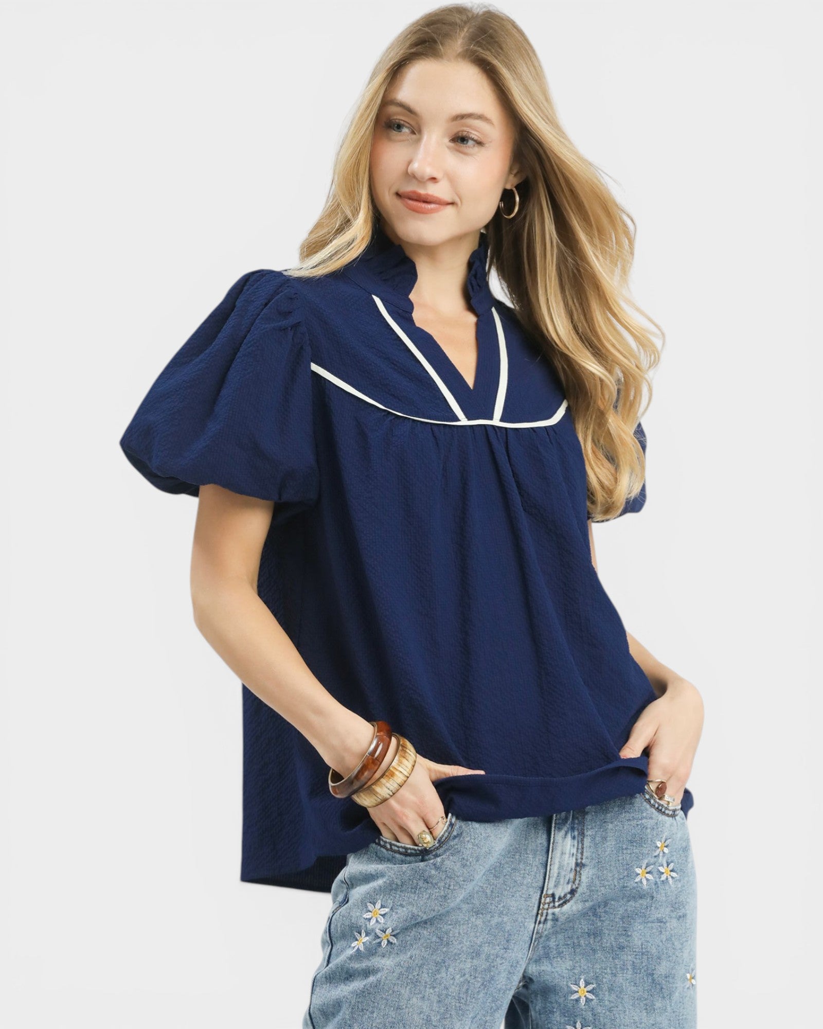 Woman wearing a navy blue blouse with white trim and jeans on a light gray background