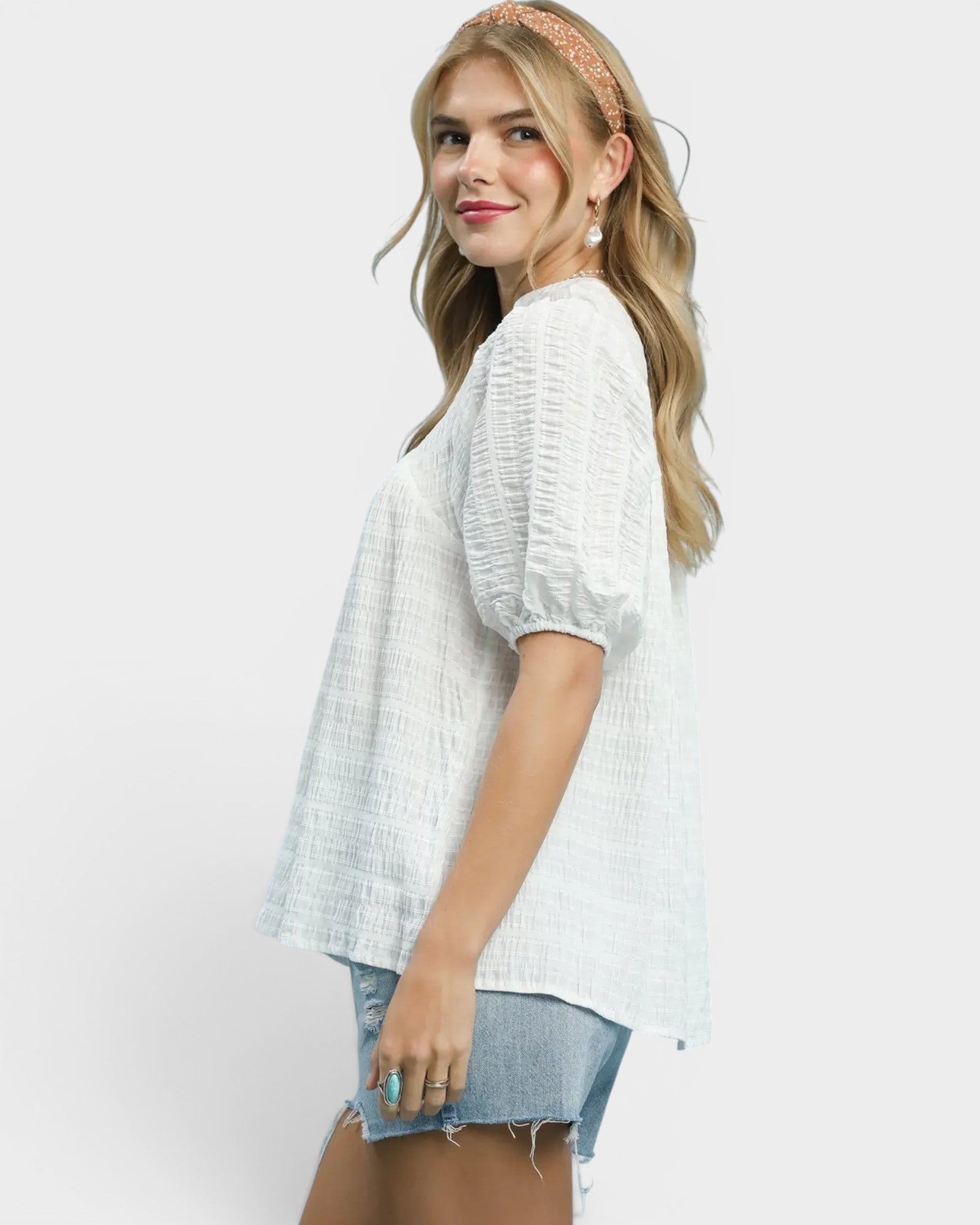 Woman wearing a white textured top and denim shorts on a plain background