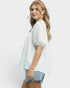 Woman wearing a white textured top and denim shorts on a plain background