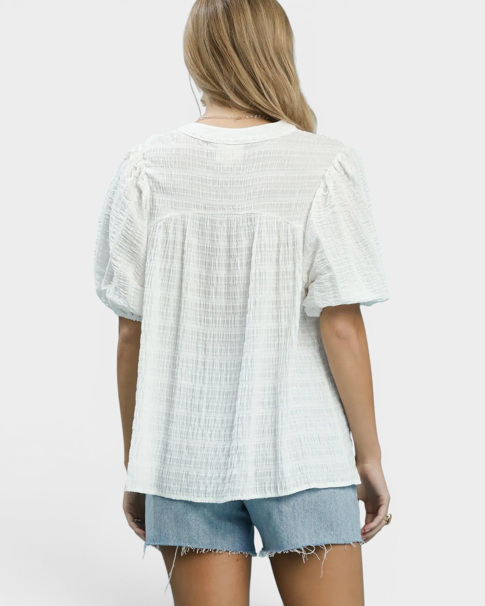 Person wearing a light-colored textured blouse and denim shorts on a white background
