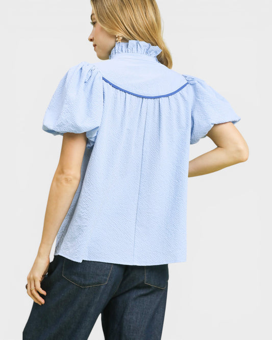 Woman wearing a light blue blouse with ruffled sleeves on a plain background