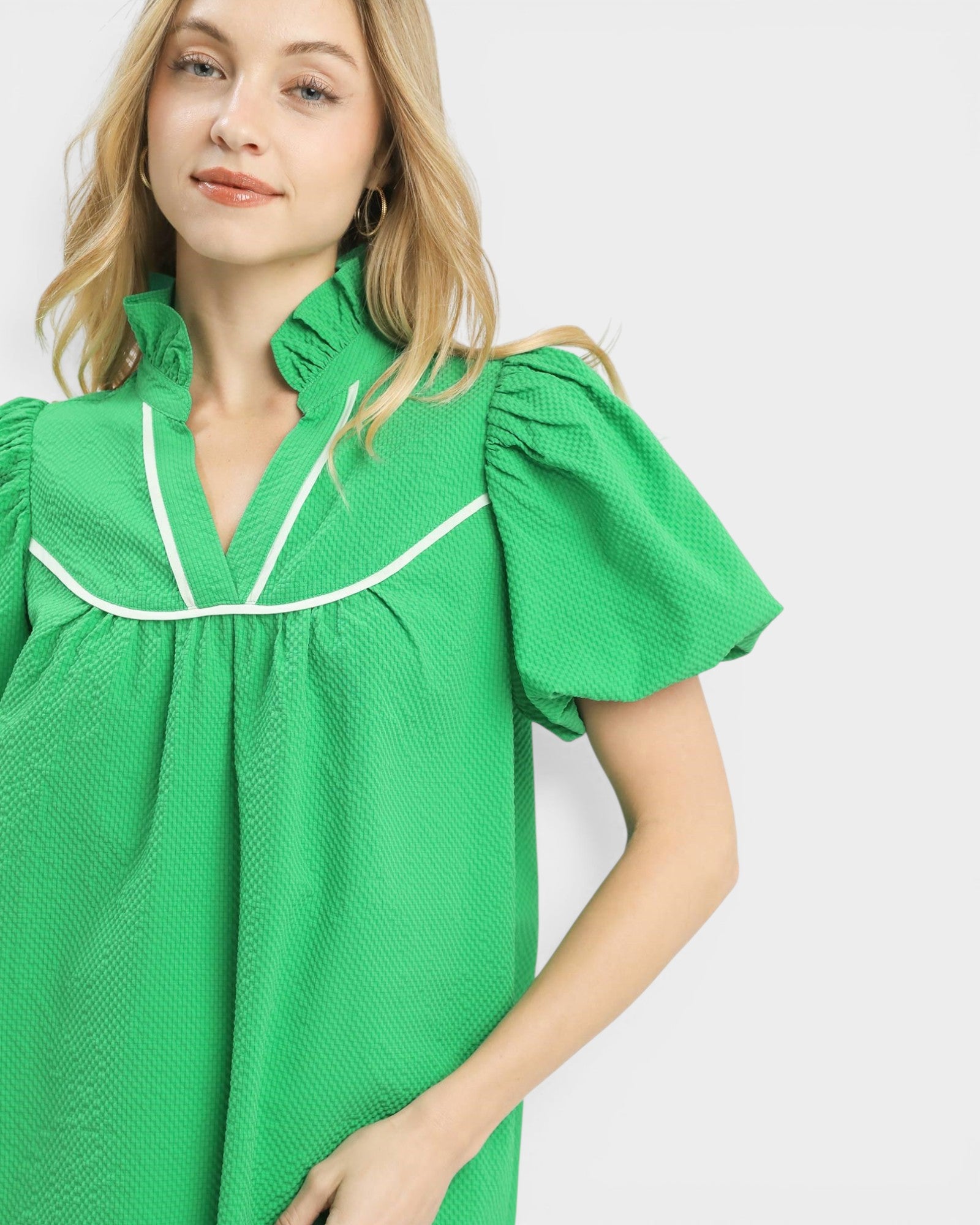 Woman wearing a green blouse with white trim on a plain background
