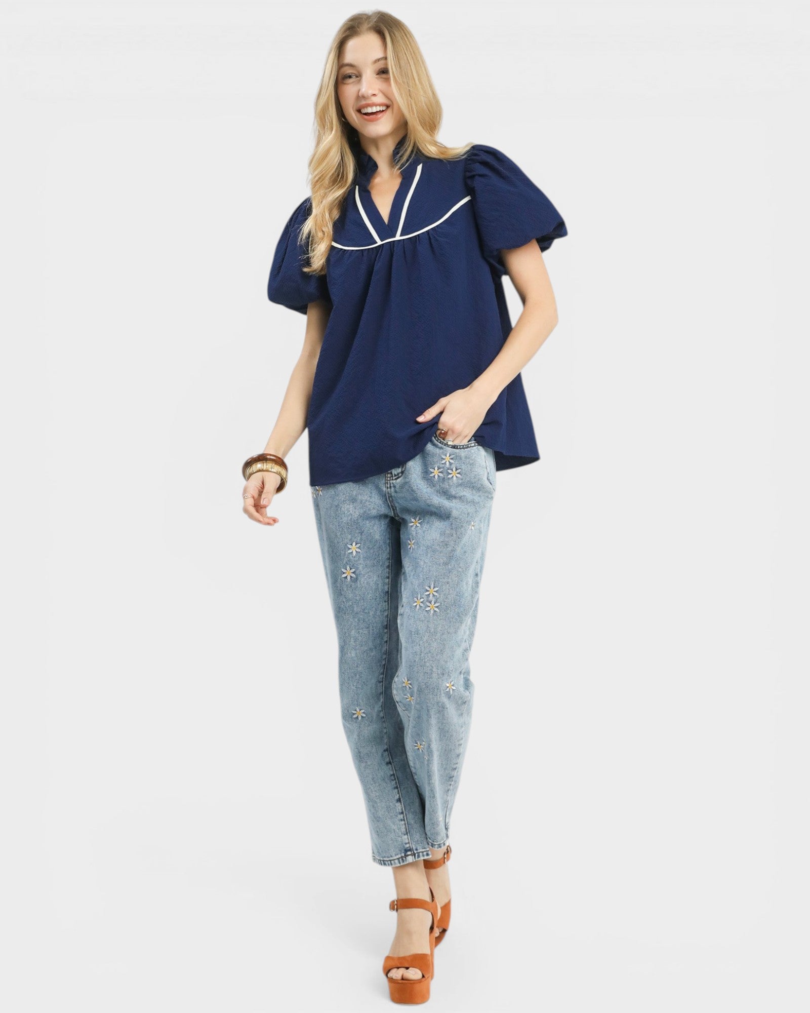 Woman wearing a navy blue blouse with white trim and light blue jeans on a white background