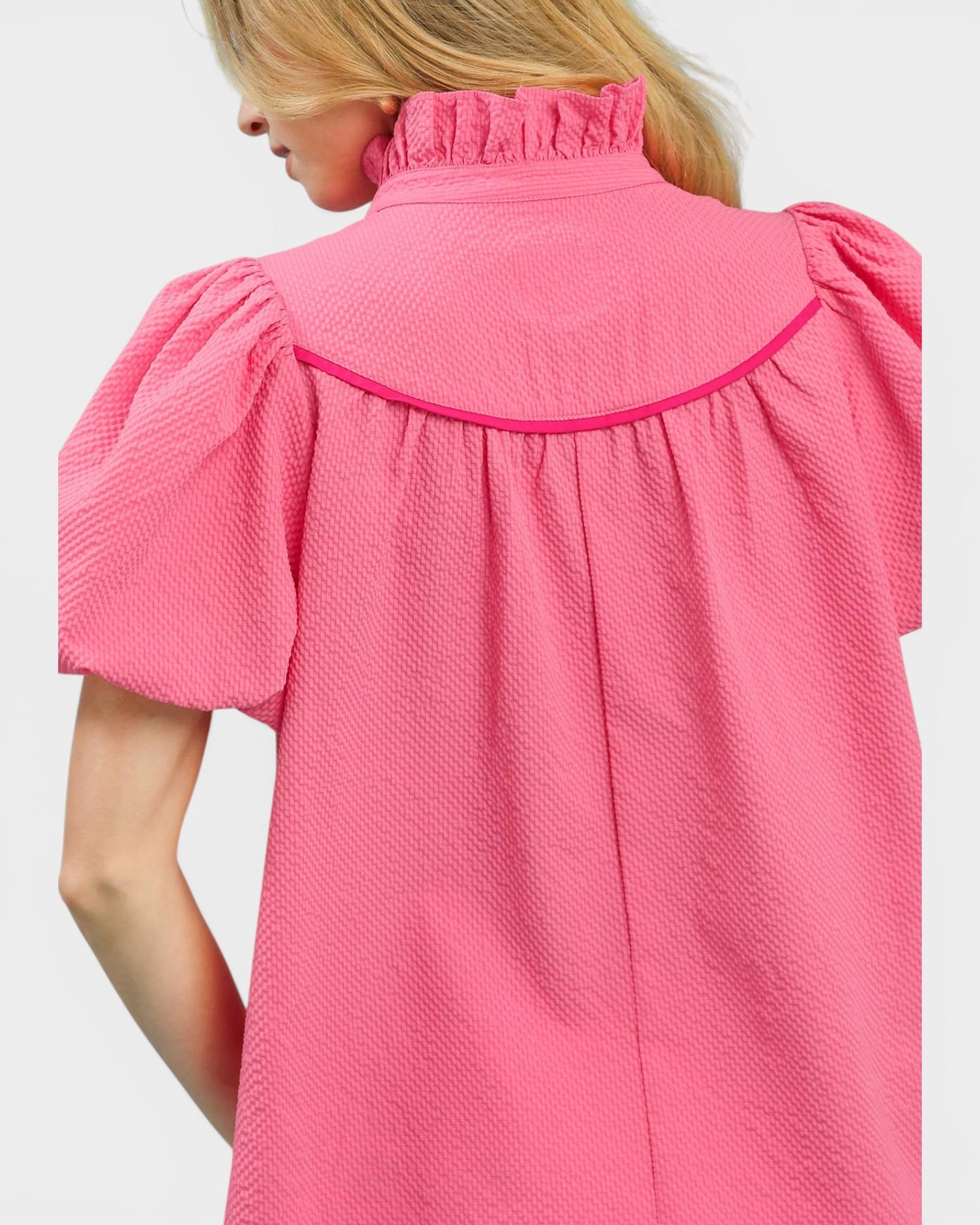 Close-up of a pink textured dress with ruffled shoulders on a white background