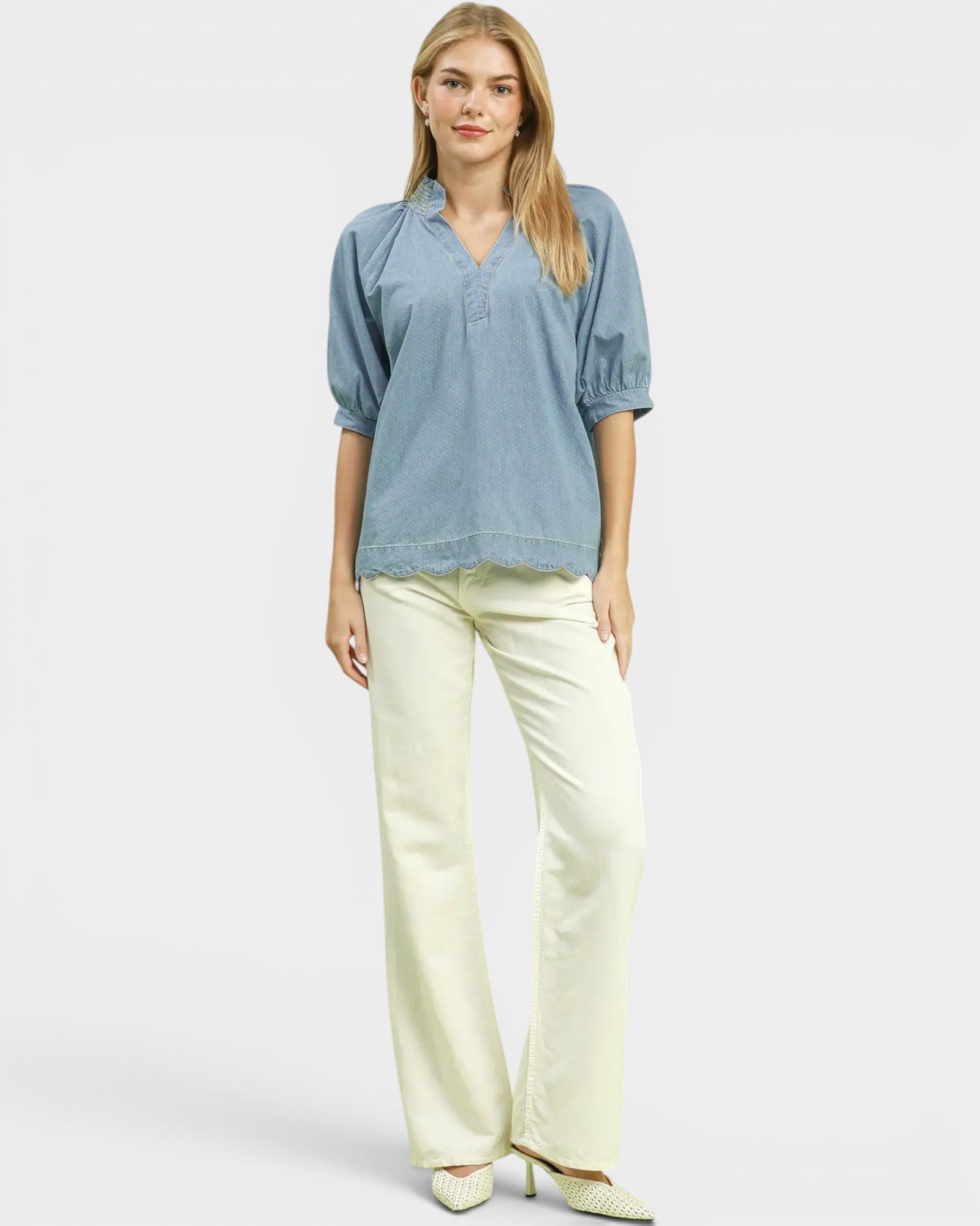 Woman wearing a blue blouse and cream pants on a white background