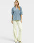 Woman wearing a blue blouse and cream pants on a white background