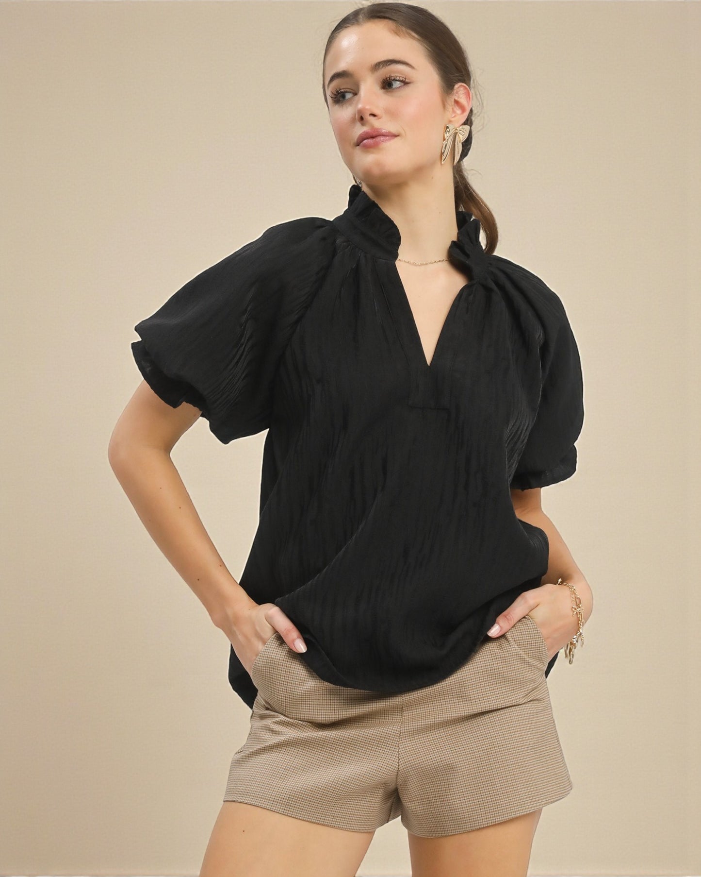 Woman wearing a black top and beige shorts against a beige background