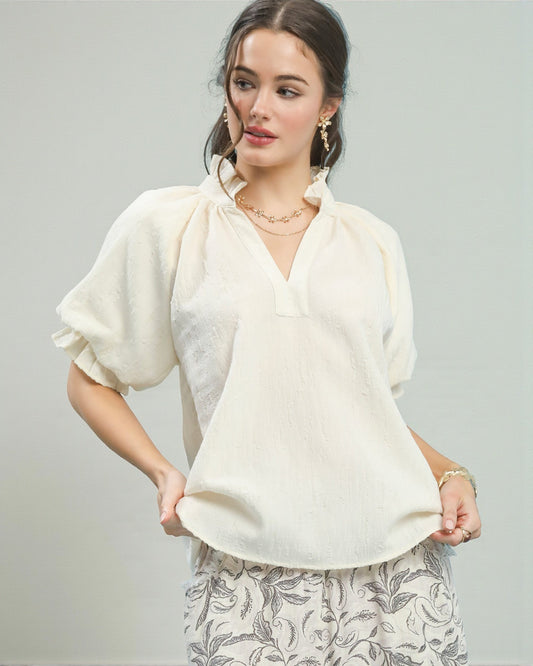 Woman wearing a white blouse with ruffled sleeves against a gray background