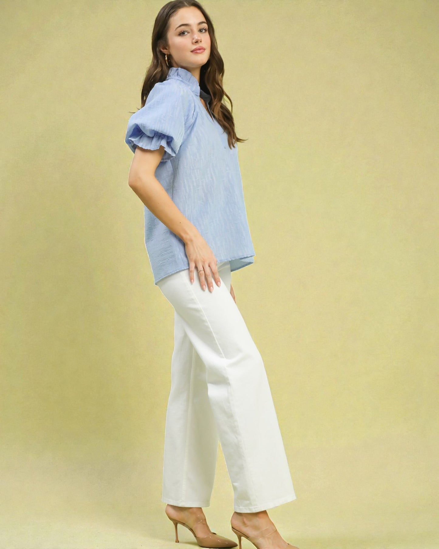 Woman wearing a light blue blouse and white pants against a yellow background