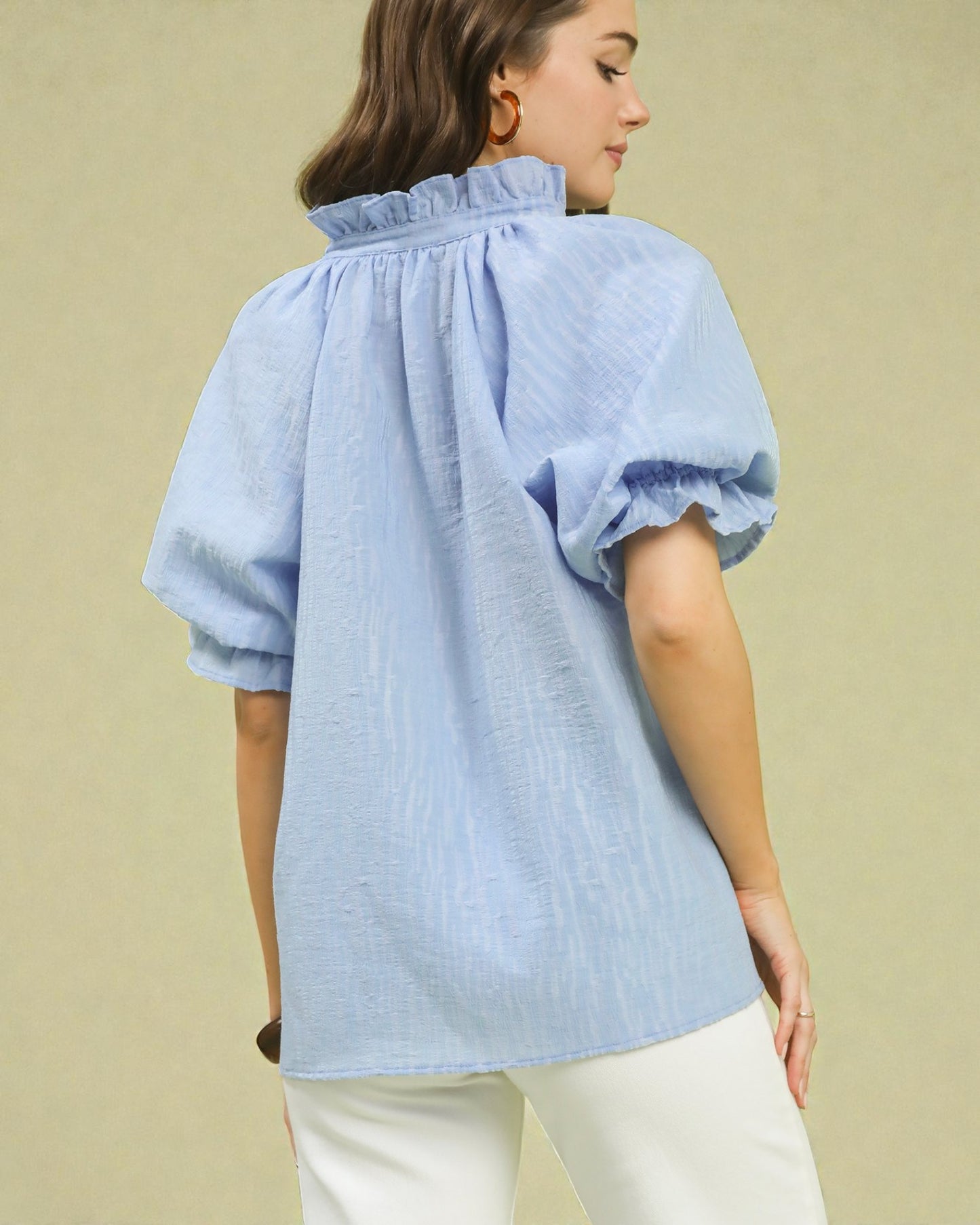 Woman wearing a light blue blouse with puff sleeves on a beige background