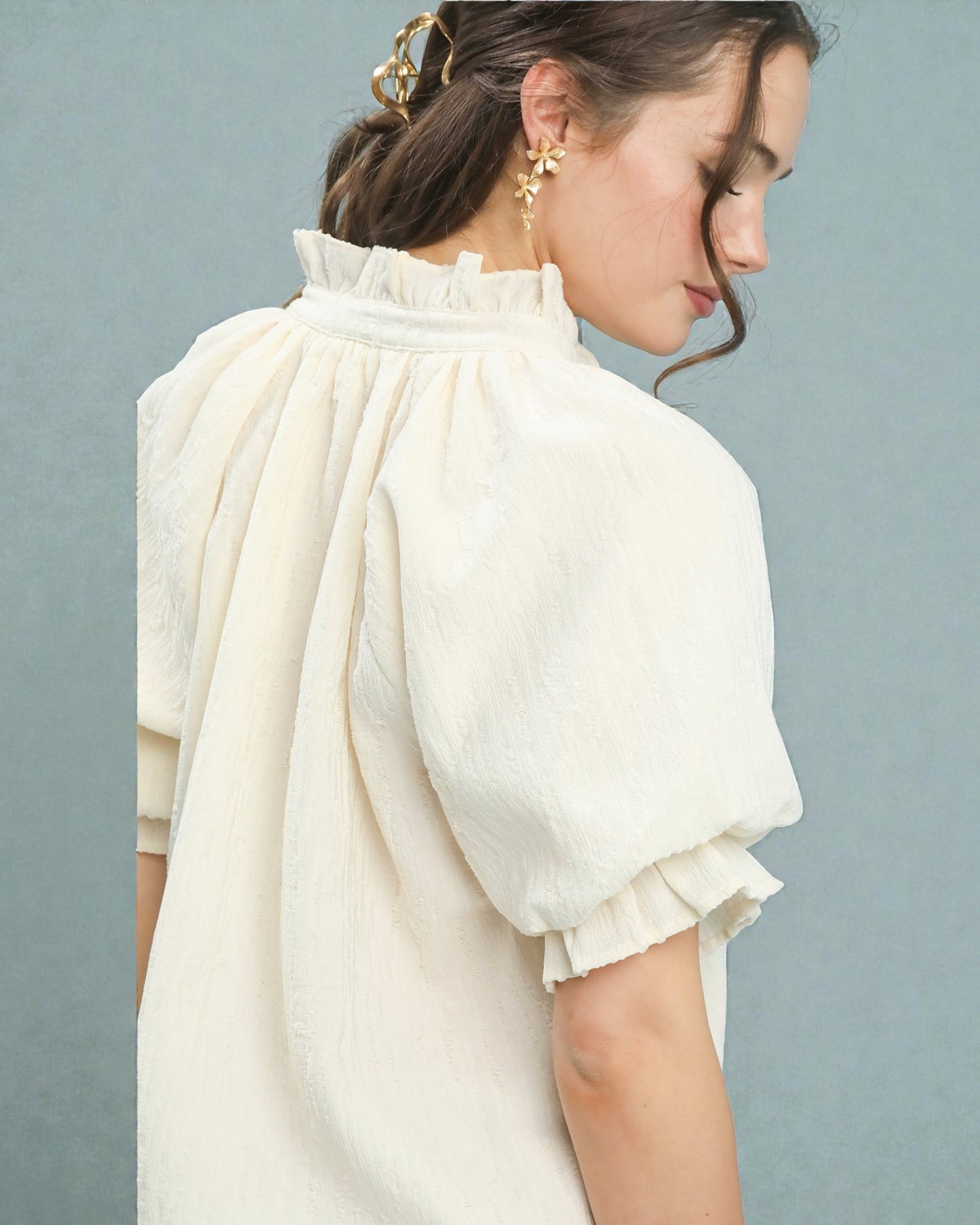 Woman wearing a cream-colored blouse with ruffled sleeves against a light blue background