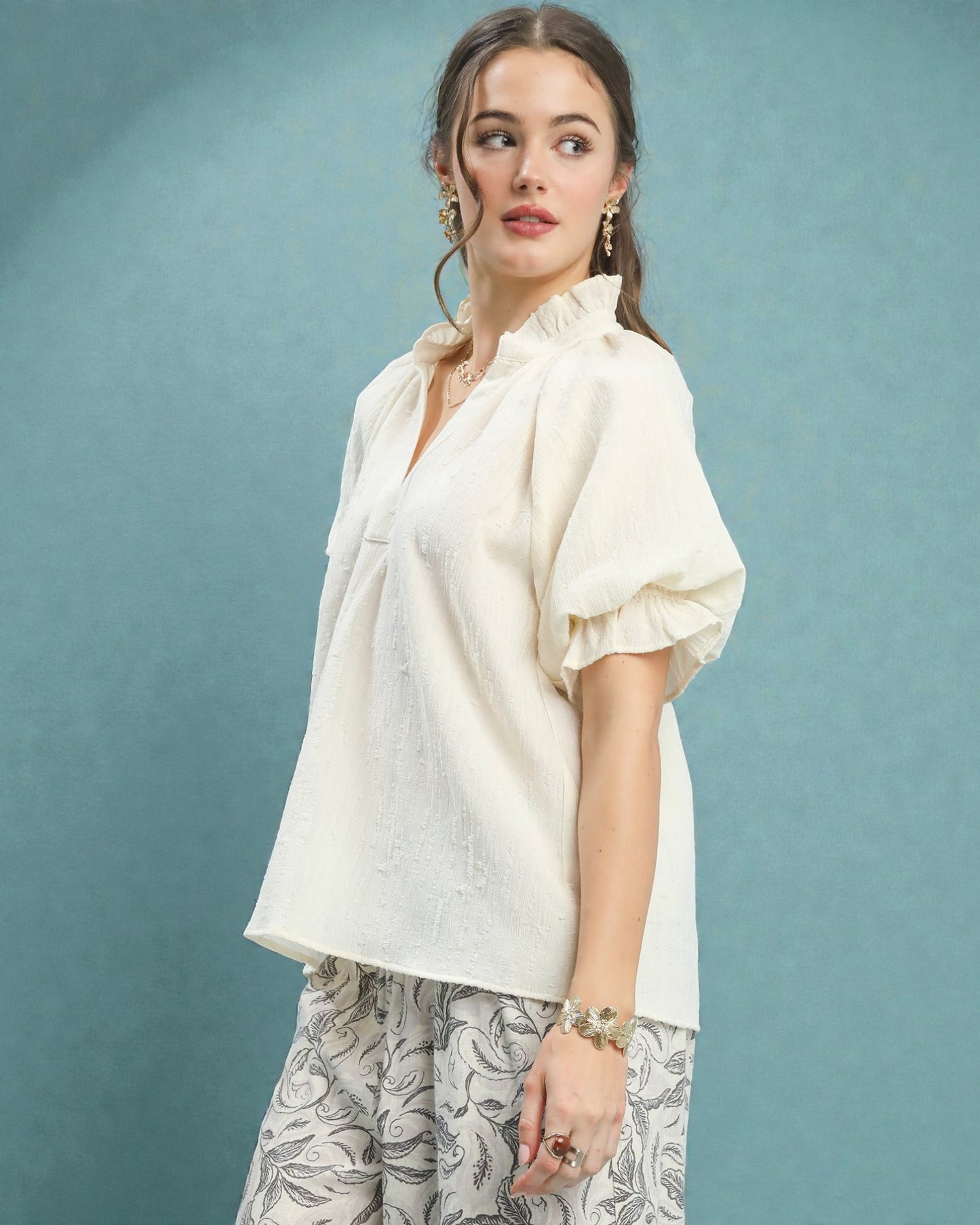 Woman wearing a white blouse with puff sleeves against a teal background