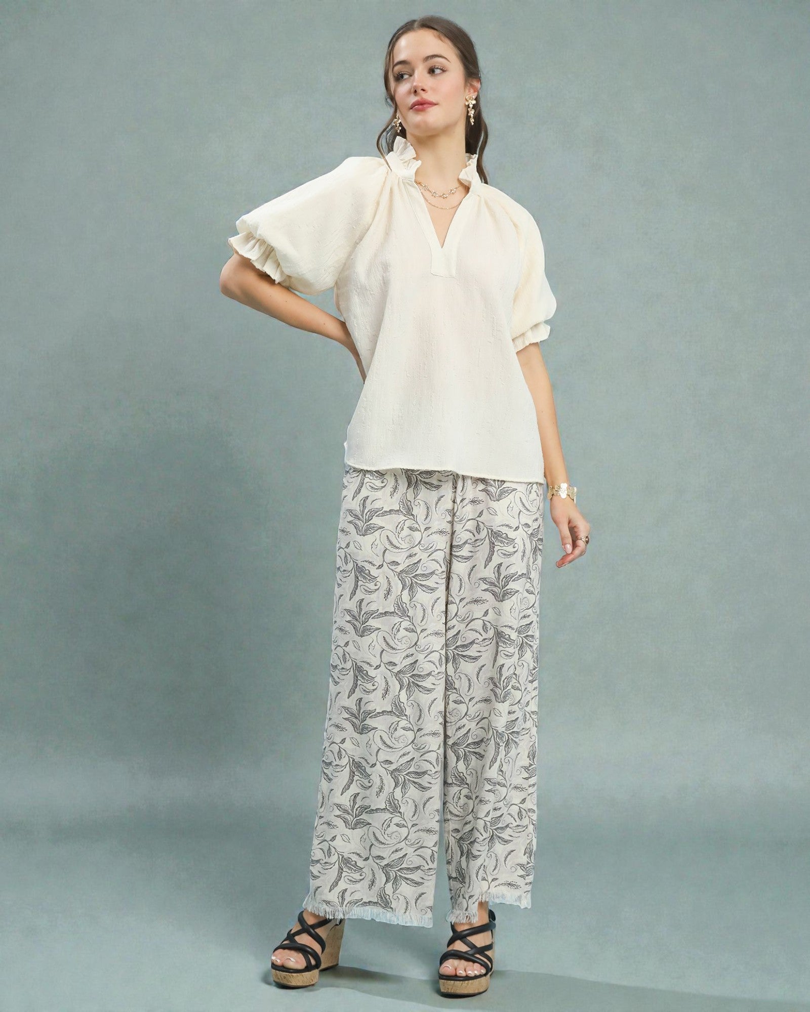 Woman wearing a white blouse and patterned pants on a gray background