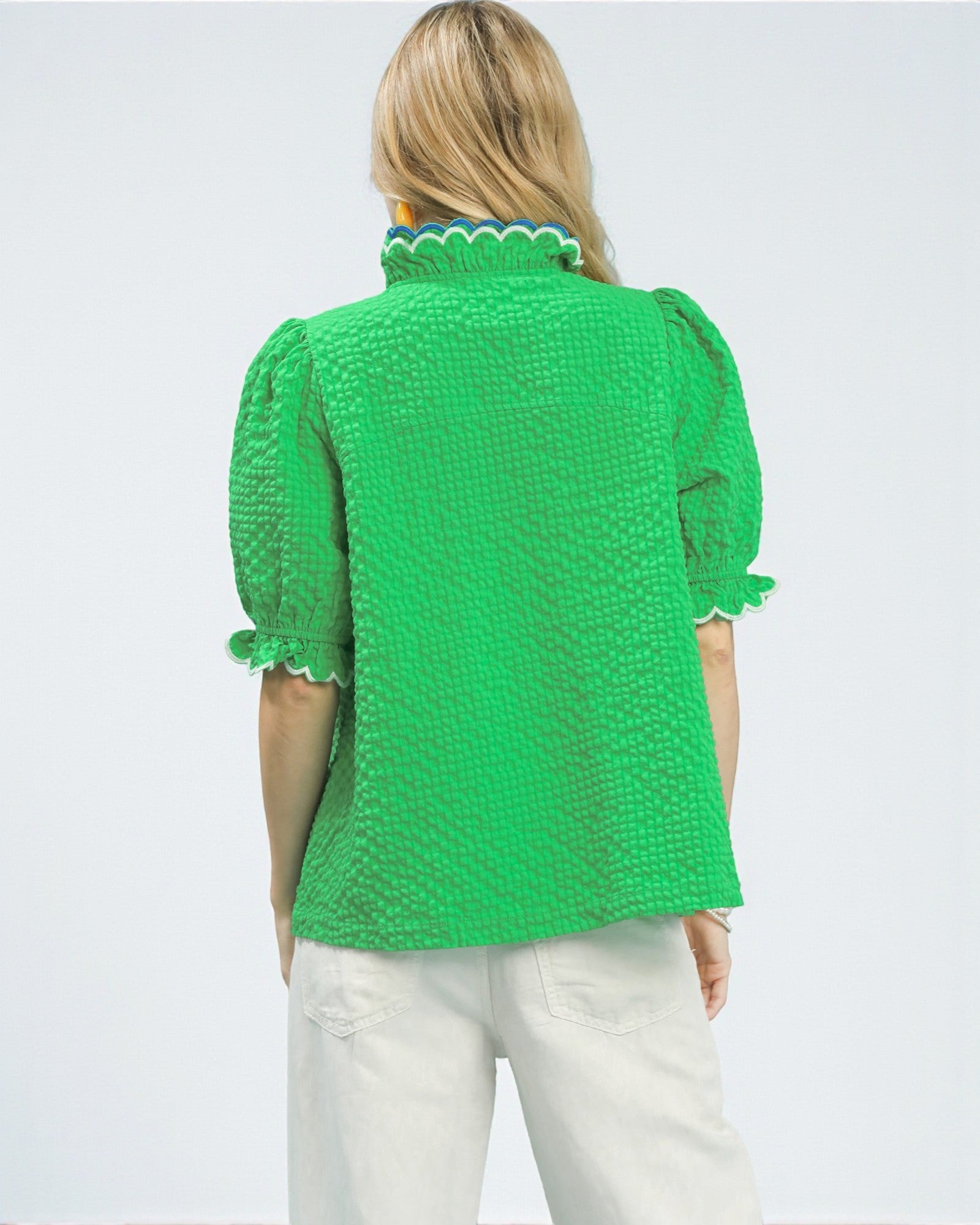 Green textured blouse with scalloped trim worn by a person on a light gray background