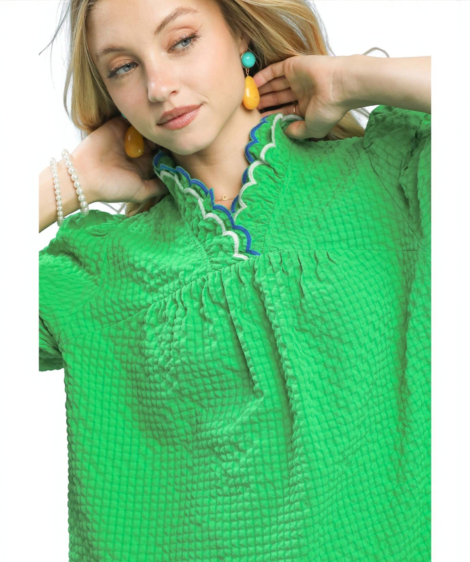 Woman wearing a green textured top with colorful earrings on a white background