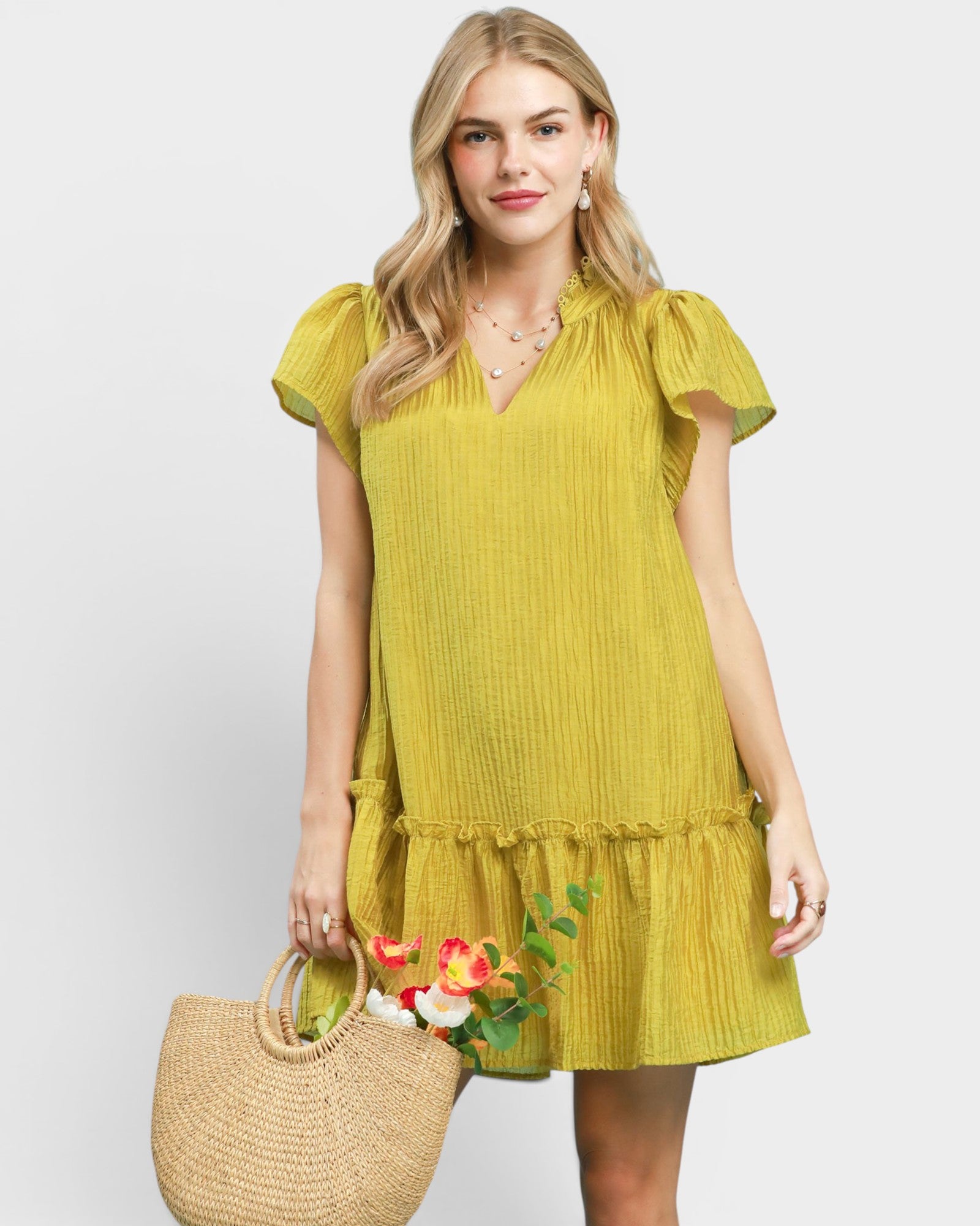 Woman wearing a yellow dress holding a straw bag with flowers on a white background