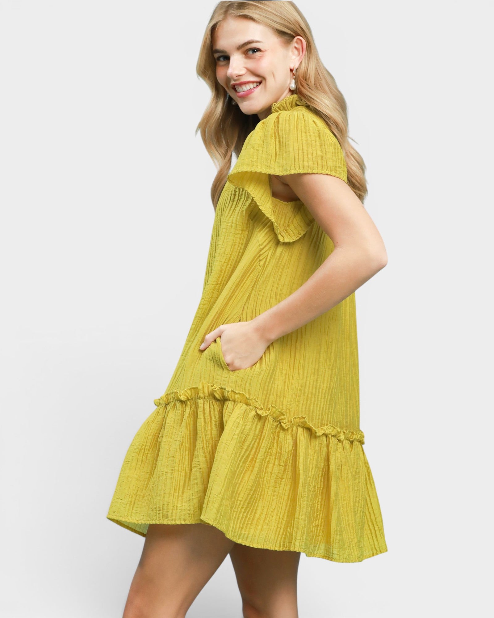 Woman wearing a yellow dress with ruffled layers on a light gray background