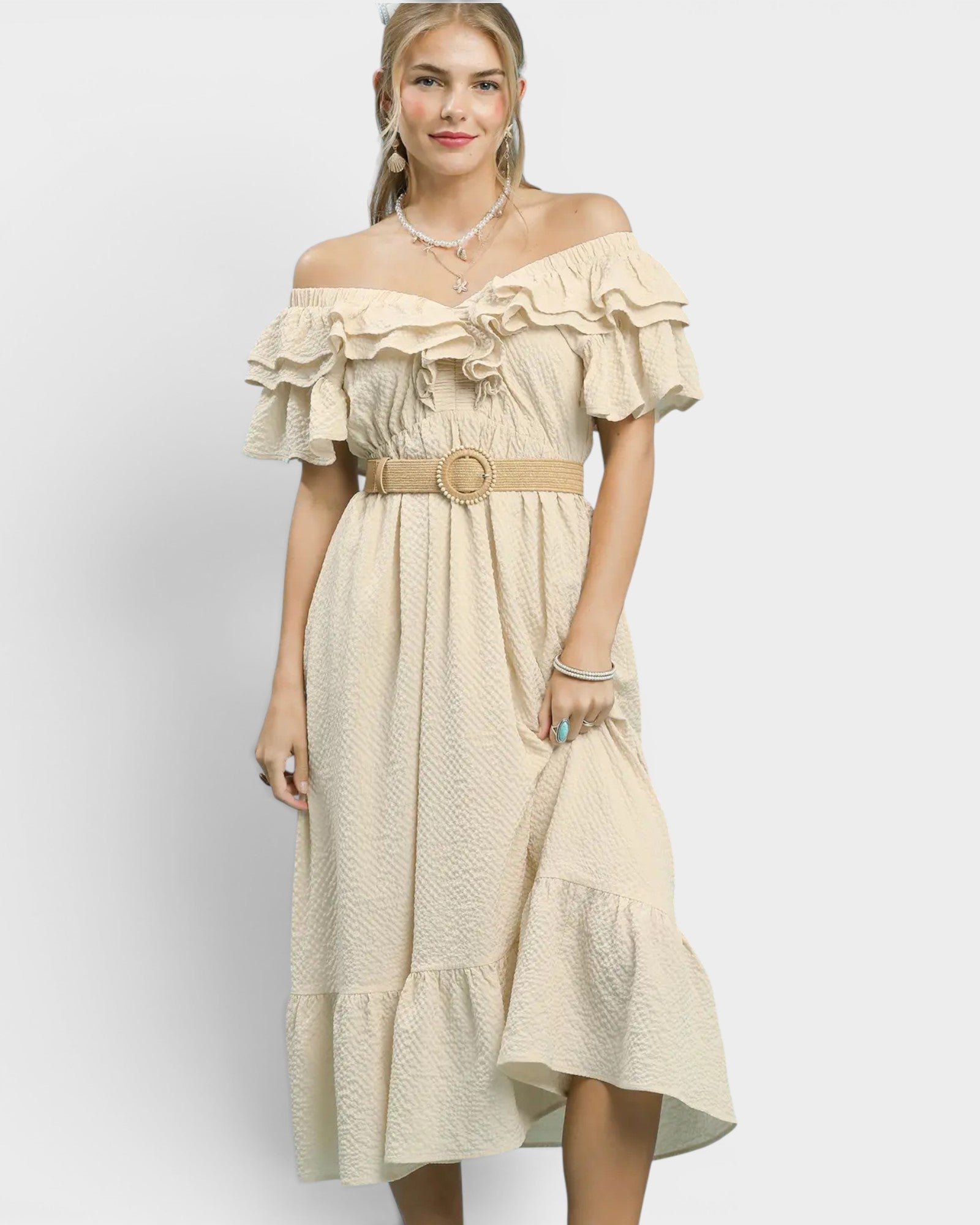 Woman wearing a beige off-shoulder dress with ruffles on a white background